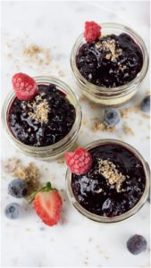 Fresh berry jam in glass jars with raspberries and blueberries, topped with crumbly streusel, on a white marble surface. Perfect for homemade desserts or breakfast spreads.