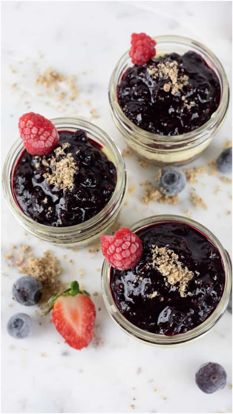 Fresh berry jam in glass jars with raspberries and blueberries, topped with crumbly streusel, on a white marble surface. Perfect for homemade desserts or breakfast spreads.