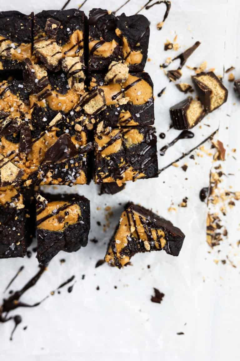 Decadent chocolate peanut butter bars topped with chocolate drizzle, crushed graham crackers, and sea salt on parchment paper, perfect for dessert or sweet snack indulgence.