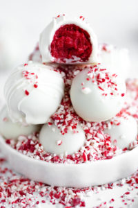 Creamy white chocolate truffles topped with crushed peppermint candies and one bitten berry-flavored truffle showing a vibrant red interior, perfect for holiday desserts.