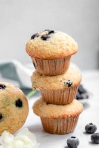 Fresh blueberry muffins stacked on a white marble surface with blueberries scattered around, showcasing delicious homemade blueberry muffins with moist texture and ripe blueberries, perfect for breakfast or snacks.