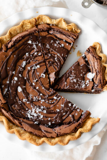 Rich chocolate tart with flaky crust and chocolate ganache filling, topped with sea salt flakes, served on a white plate. Perfect for dessert lovers and chocolate enthusiasts.