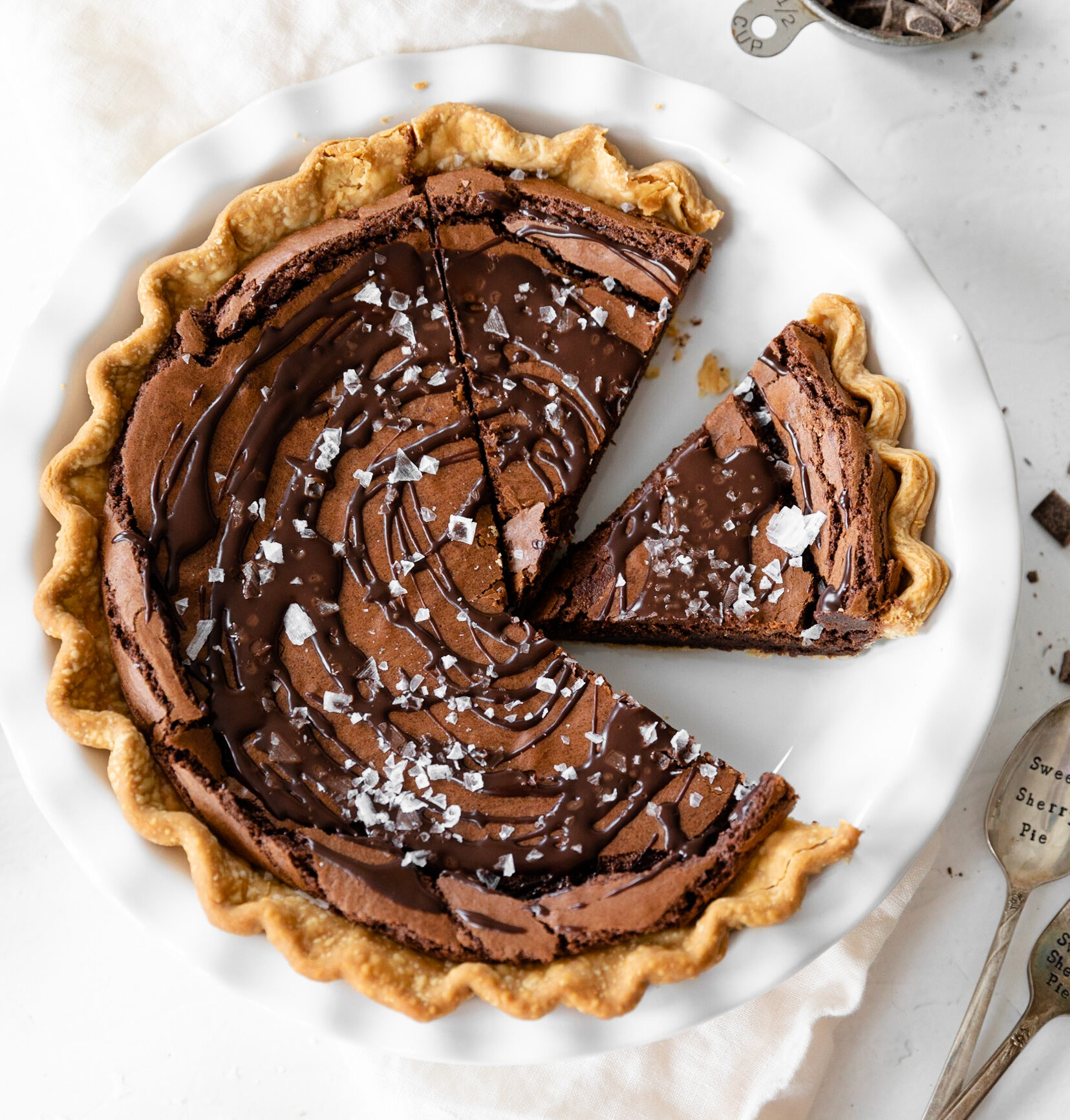 Rich chocolate tart with flaky crust and chocolate ganache filling, topped with sea salt flakes, served on a white plate. Perfect for dessert lovers and chocolate enthusiasts.
