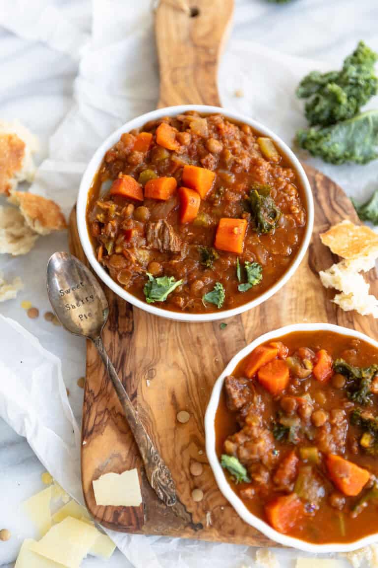 Hearty homemade beef vegetable stew in white bowls on a wooden serving board, featuring carrots, potatoes, and beef, served with bread slices, perfect for comfort food lovers.
