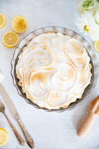 Lemon meringue pie topped with toasted meringue, garnished with fresh lemon slices and flowers, served on a white surface, perfect for lemon dessert lovers.