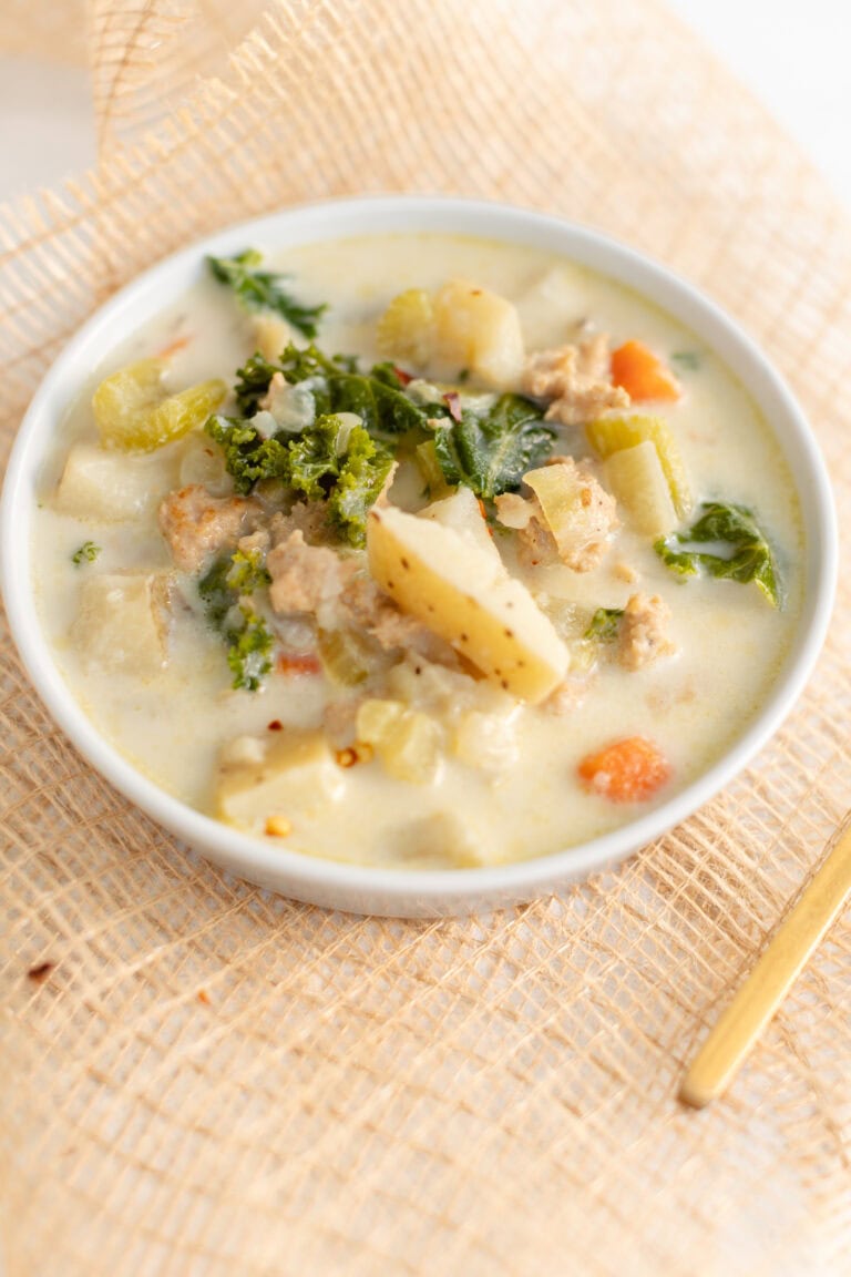 Creamy homemade potato soup garnished with fresh herbs in a white bowl on a woven placemat.