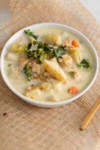 Creamy chicken pot pie soup with fresh vegetables and herbs in a white bowl on woven placemat. Perfect comfort food for the fall and winter seasons.
