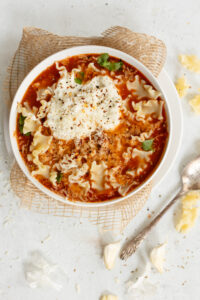 Creamy tomato-based chicken noodle soup with shredded chicken, cheese tortellini, and fresh herbs, served in a white bowl; perfect comfort food for cold days or any time.