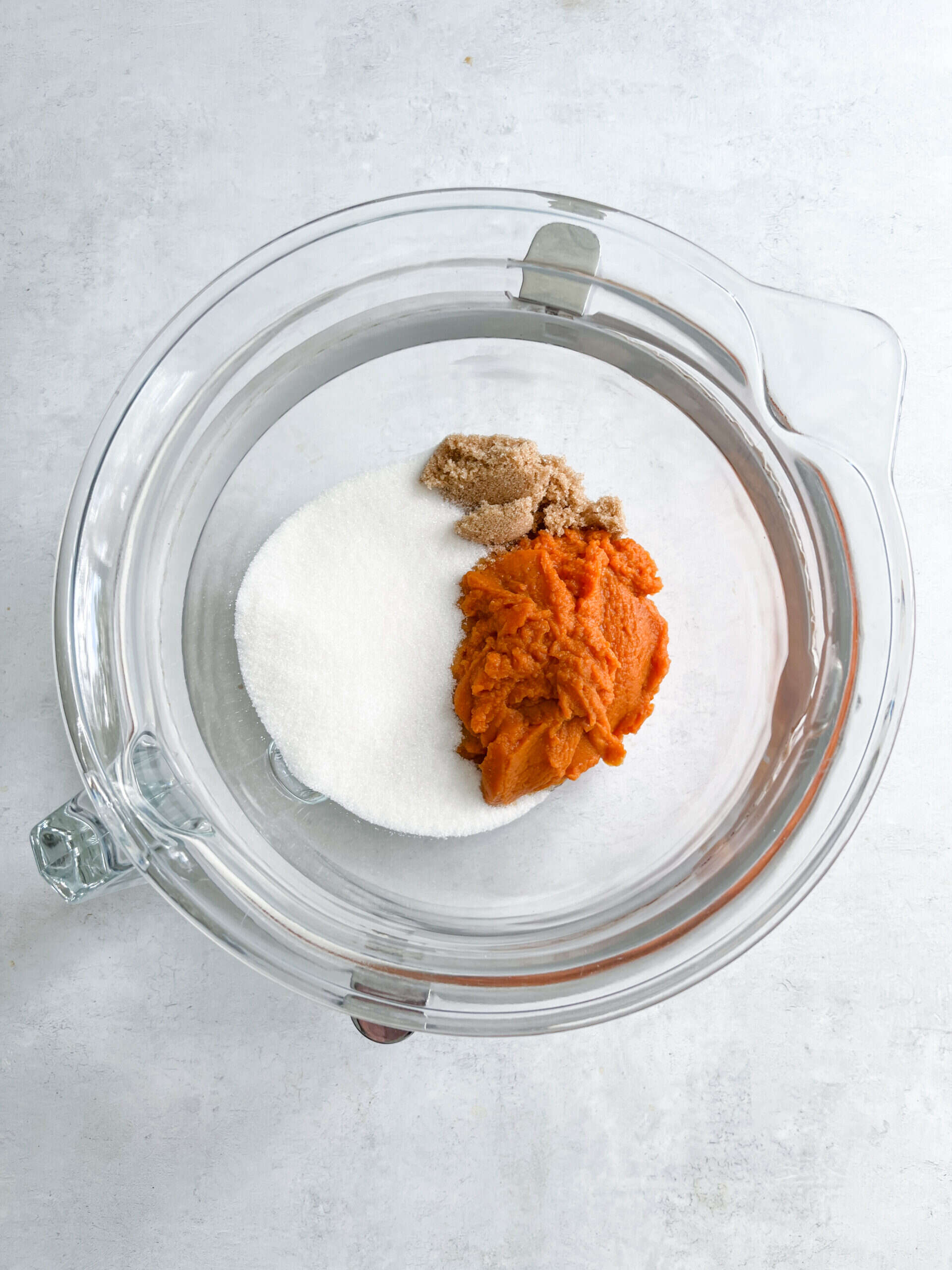 Mixed ingredients in a glass bowl for sweet potato pie, including sugar, brown sugar, and cooked sweet potatoes, ready to be blended for delicious homemade sweet potato pie.