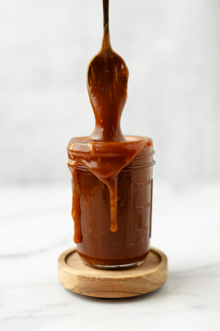 Creamy caramel sauce dripping from a spoon into a glass jar, perfect for desserts and sweet treats.