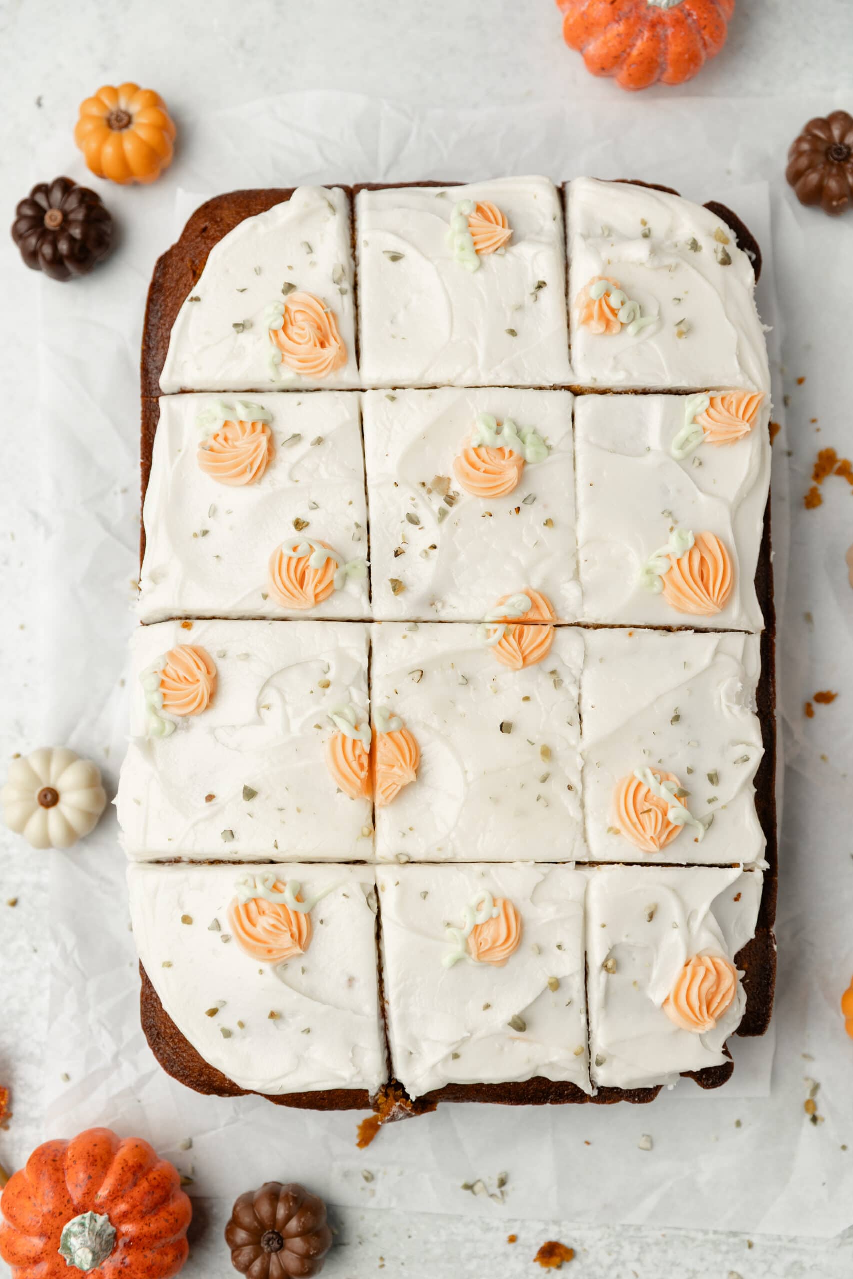 Sweet potato pie with white frosting and orange flower decorations, topped with chopped nuts, on a white surface with mini pumpkins around.